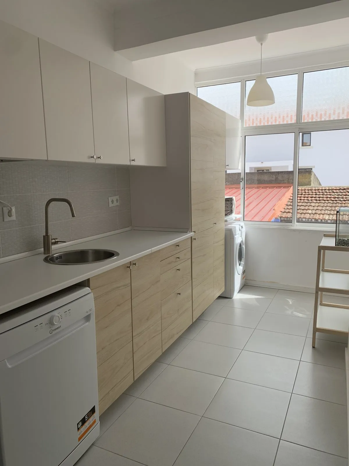 Cozinha da Alcosta renovada, com armários claros de madeira e janela para os telhados da Trafaria